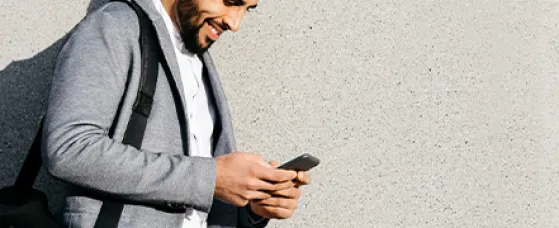 Casual young businessman using cell phone at a wall.