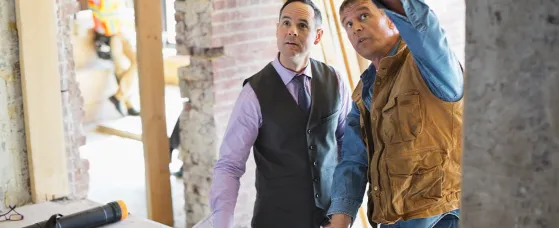 Male architect discussing blueprint with foreman at construction site.