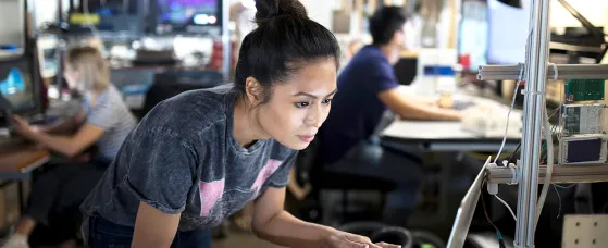 Focused female engineer working at laptop in workshop.