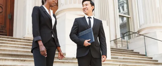 A well dressed man and woman smiling as they as they walk down steps of a courthouse building. 
