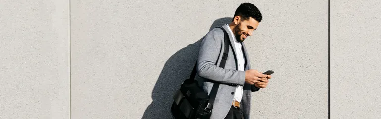 Casual young businessman using cell phone at a wall.