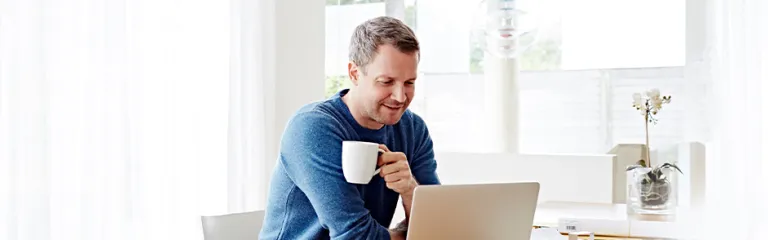 Man working at home using laptop drinking coffee