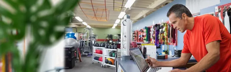 Business owner working at laptop at counter in home gym equipment store