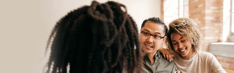 A couple sit in a nicely lit office with a mortgage personnel to discuss their loan options.