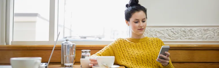 Woman texting and drinking cappuccino in cafe